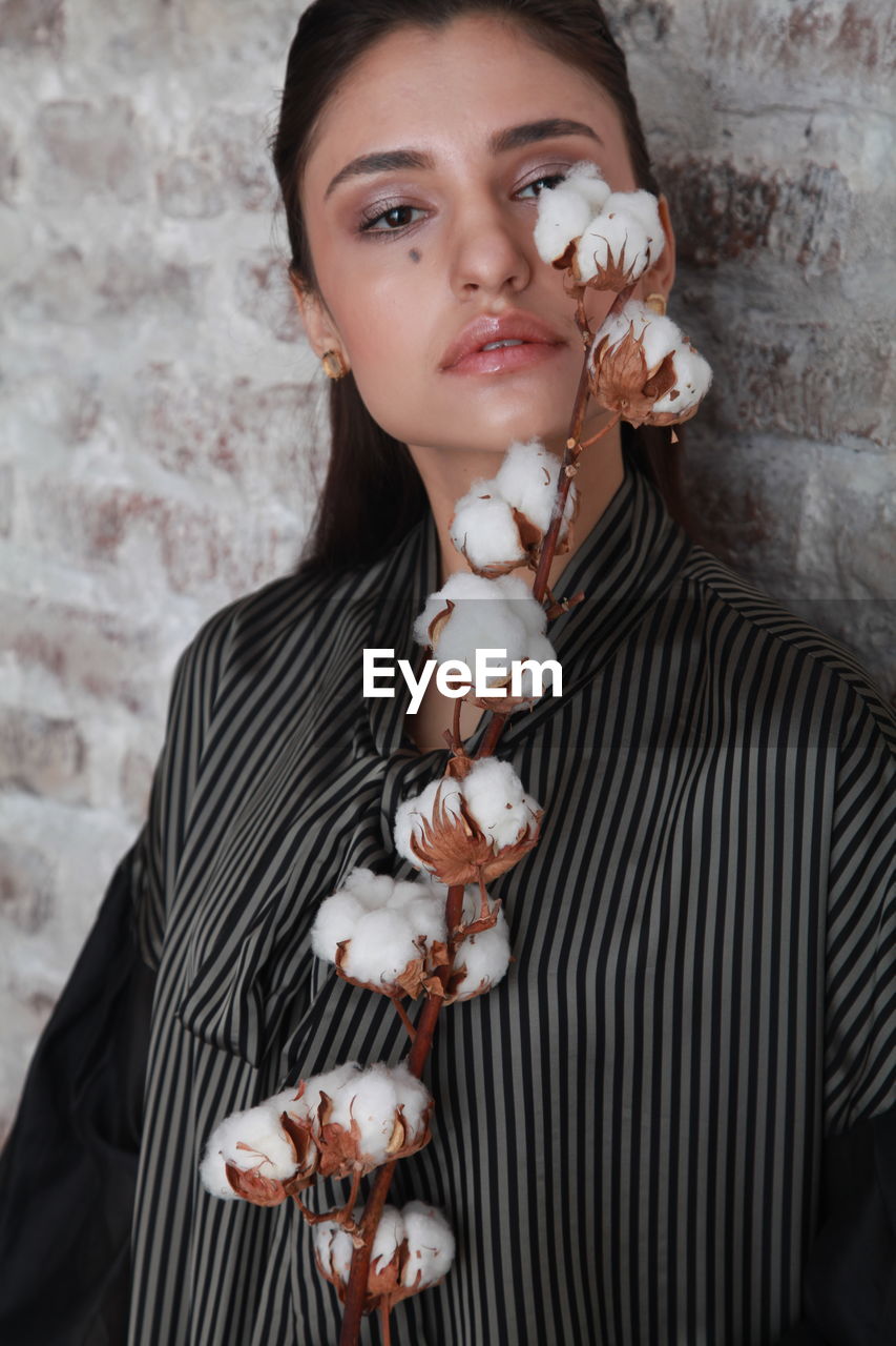 Close-up portrait of young woman holding cotton against wall