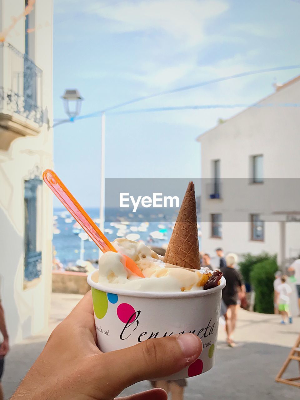 CLOSE-UP OF HAND HOLDING ICE CREAM CONE AGAINST SEA