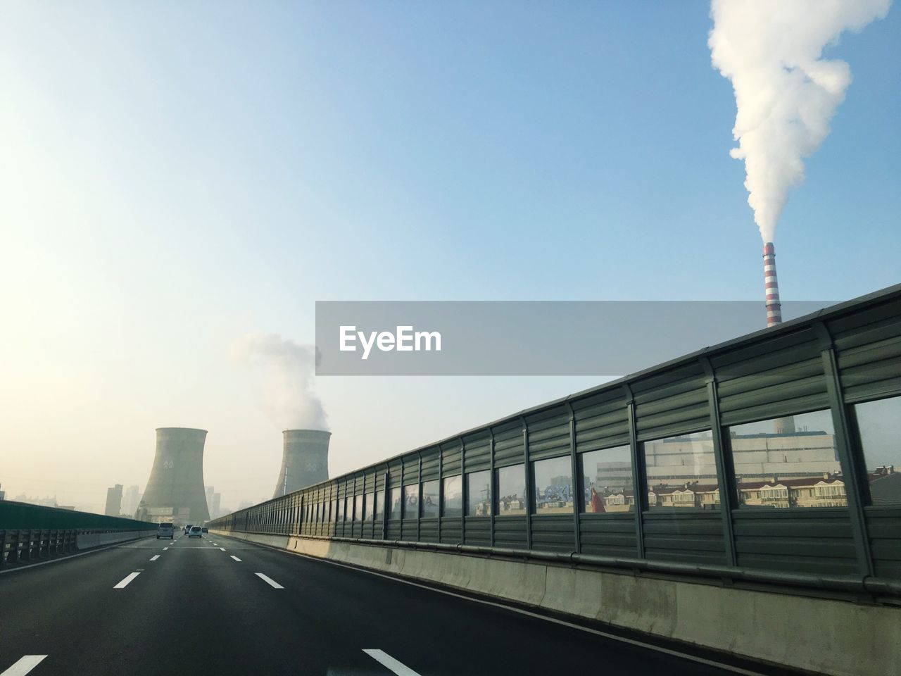 Road leading towards silos emitting smoke against clear sky