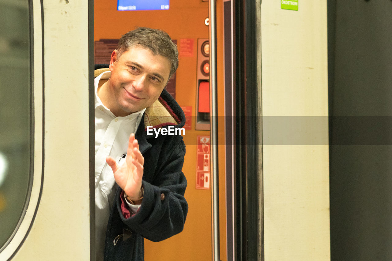 Portrait of smiling man gesturing while standing in train