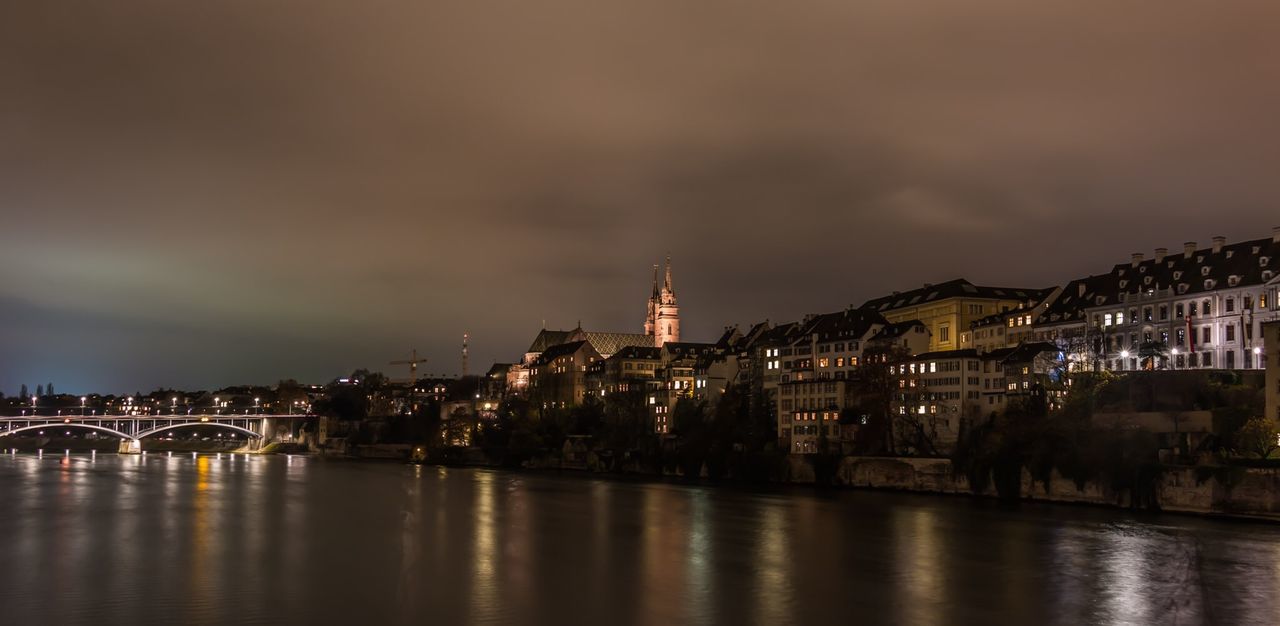 Arch bridge over river in illuminated city against sky at dusk