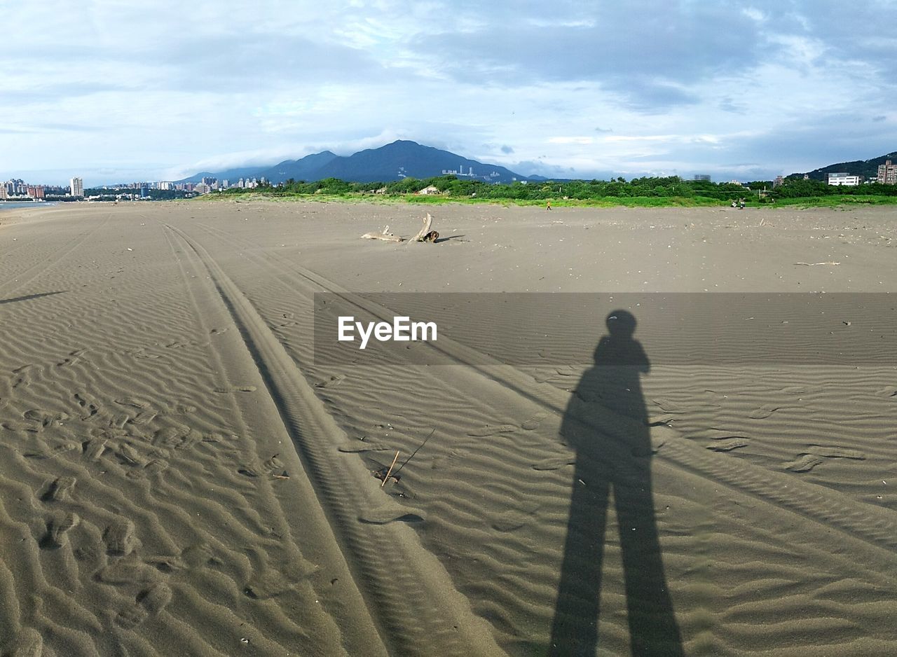 Shadow of person on sand at beach against sky