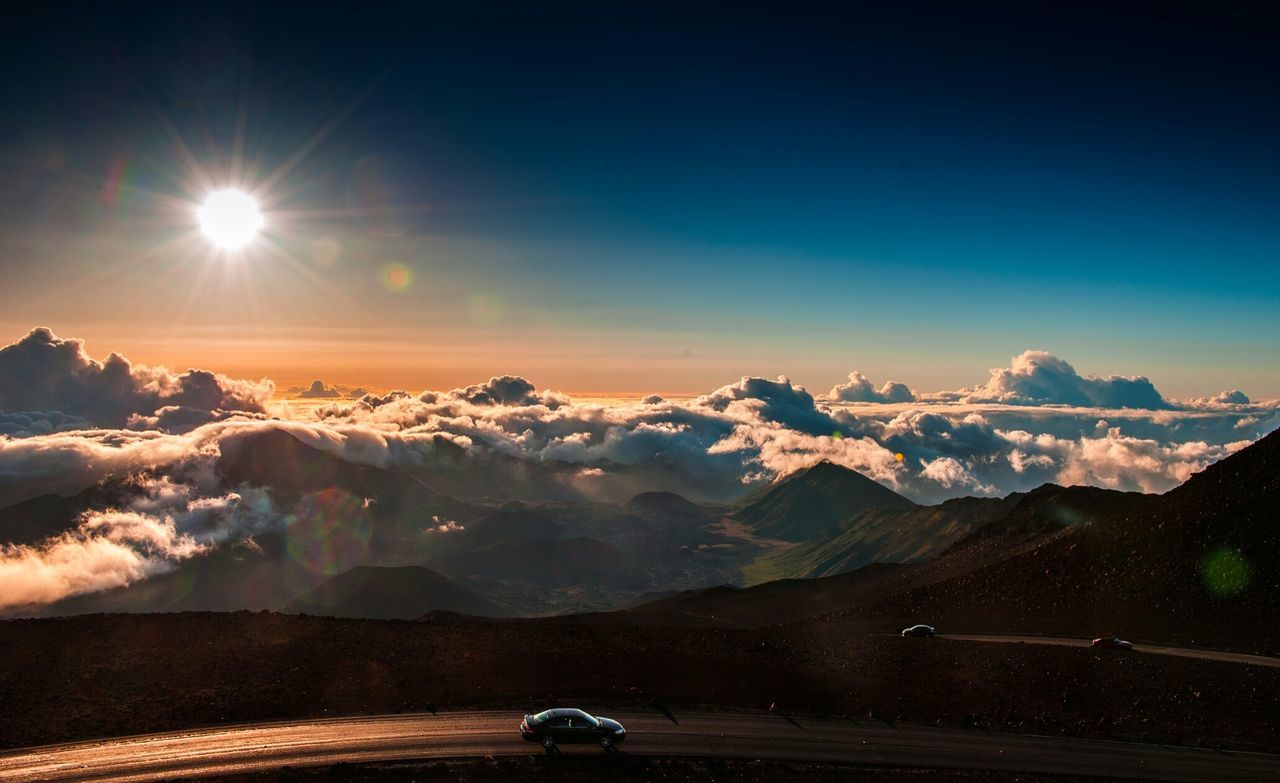 Cars on mountain road against cloudy sky