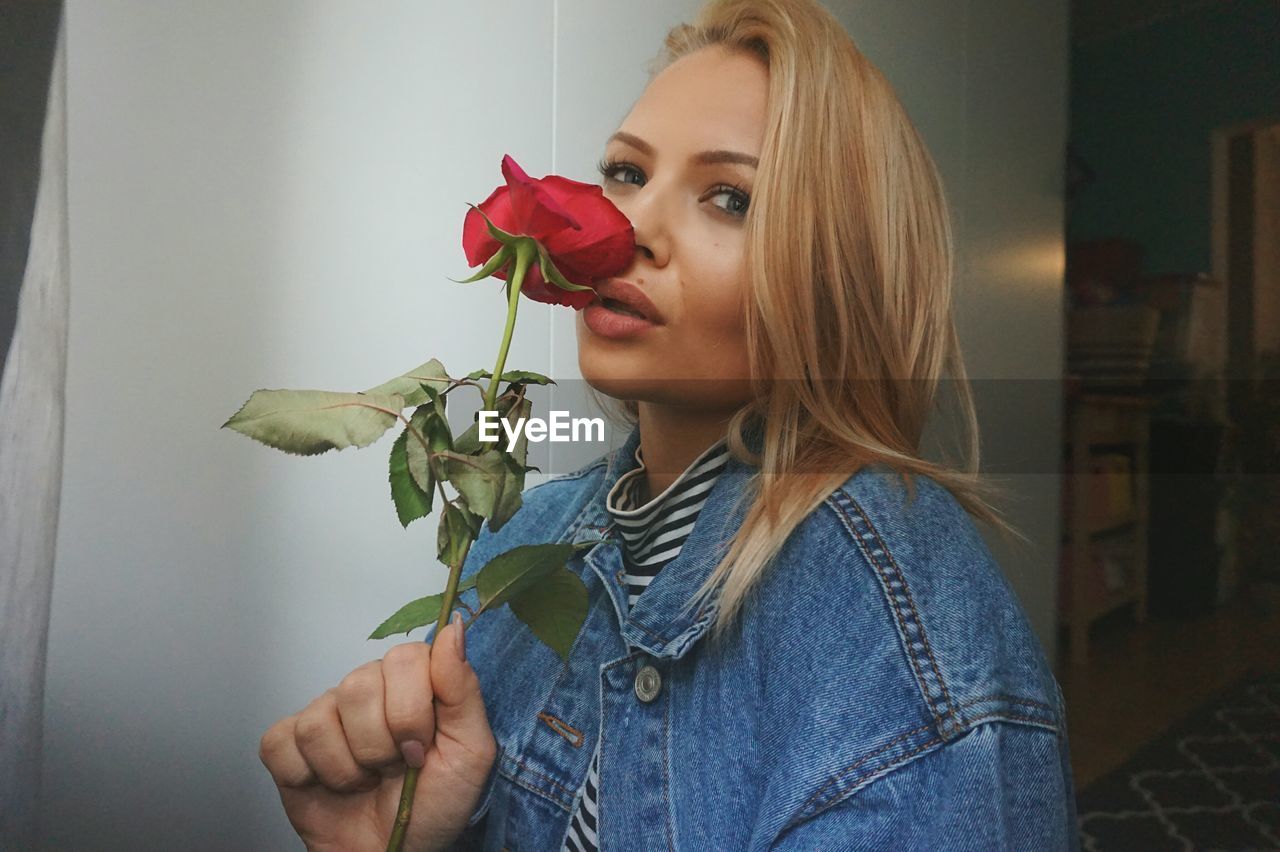 Portrait of woman holding red rose at home