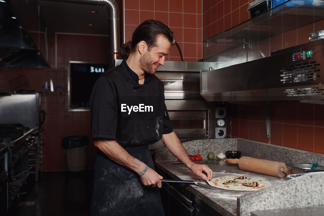 Side view of male shed  working in kitchen making a pizza