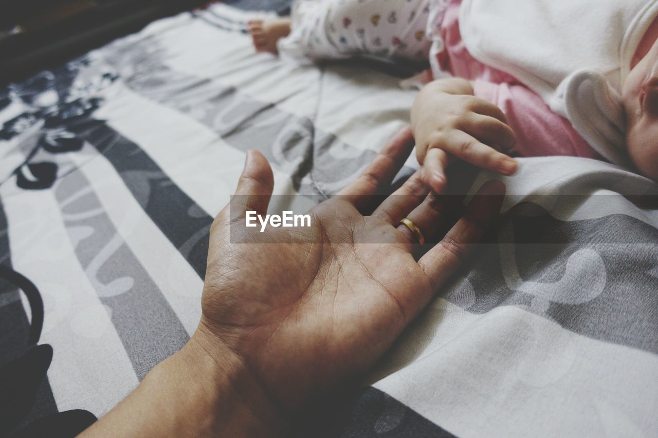 Baby holding father hand on bed at home