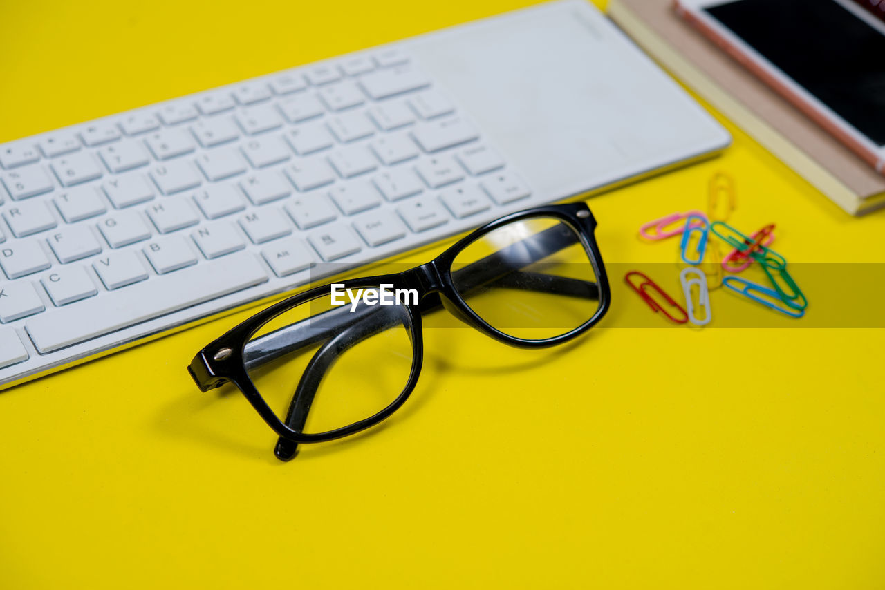 HIGH ANGLE VIEW OF EYEGLASSES ON TABLE AGAINST YELLOW BACKGROUND