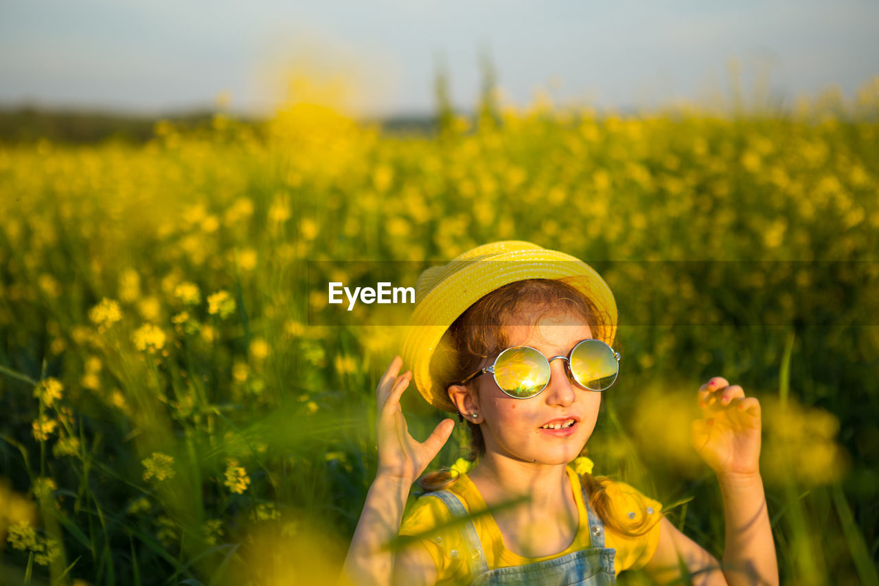 PORTRAIT OF CUTE GIRL WITH YELLOW FLOWERS IN FIELD