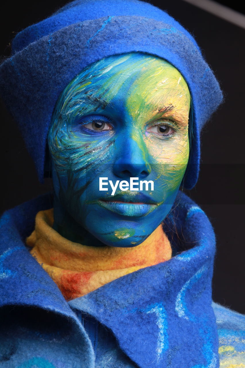 Close-up of young woman with painted face against black background