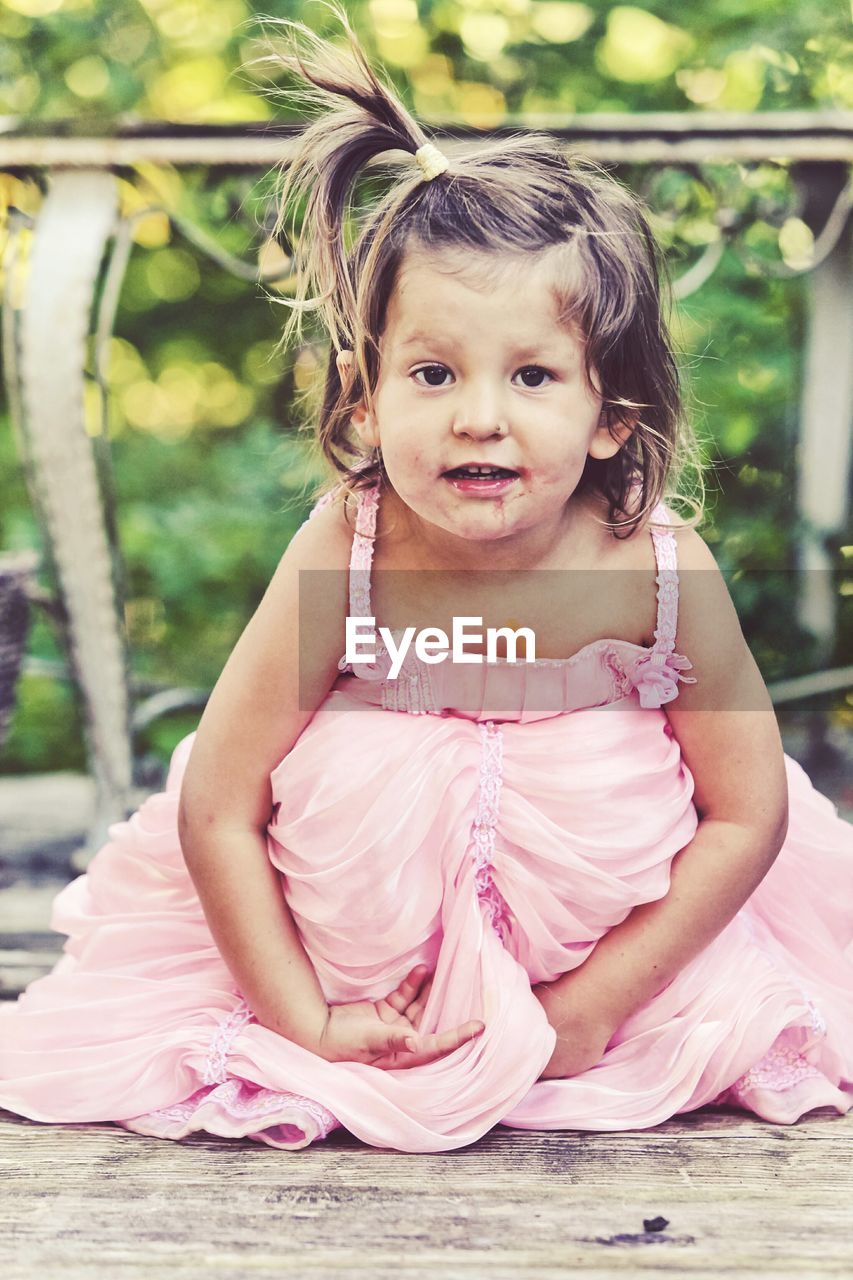 Portrait of cute girl wearing pink dress at wooden plank