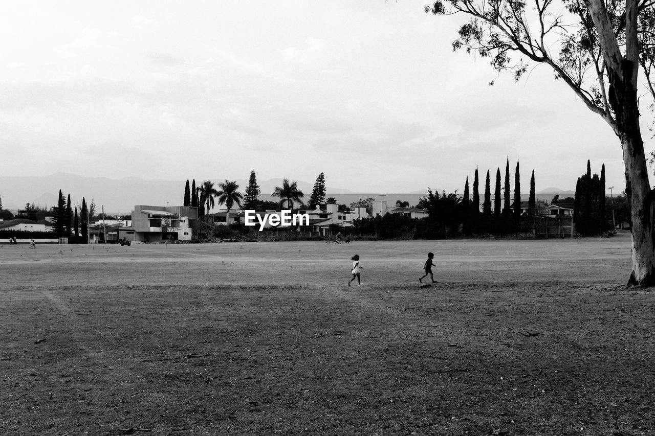 Siblings running on park against sky