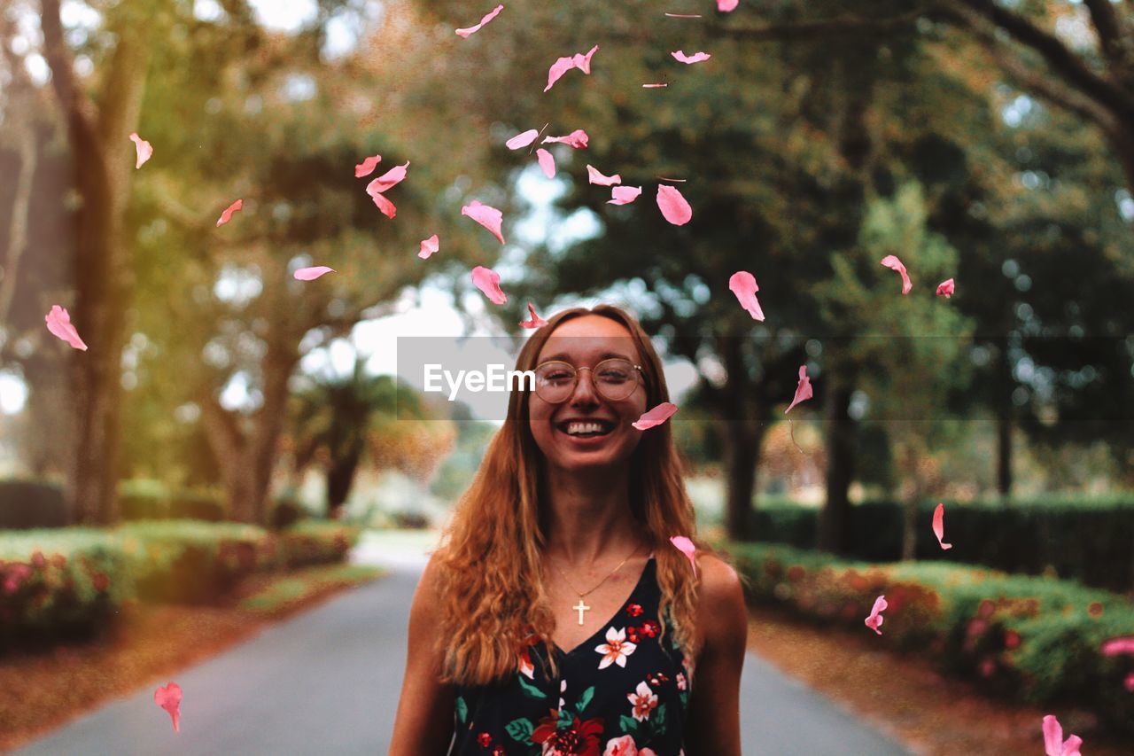 Portrait of young woman throwing petal mid-air while standing at park