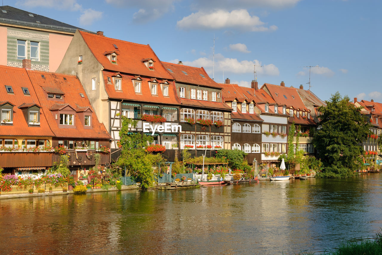 Houses at waterfront against cloudy sky