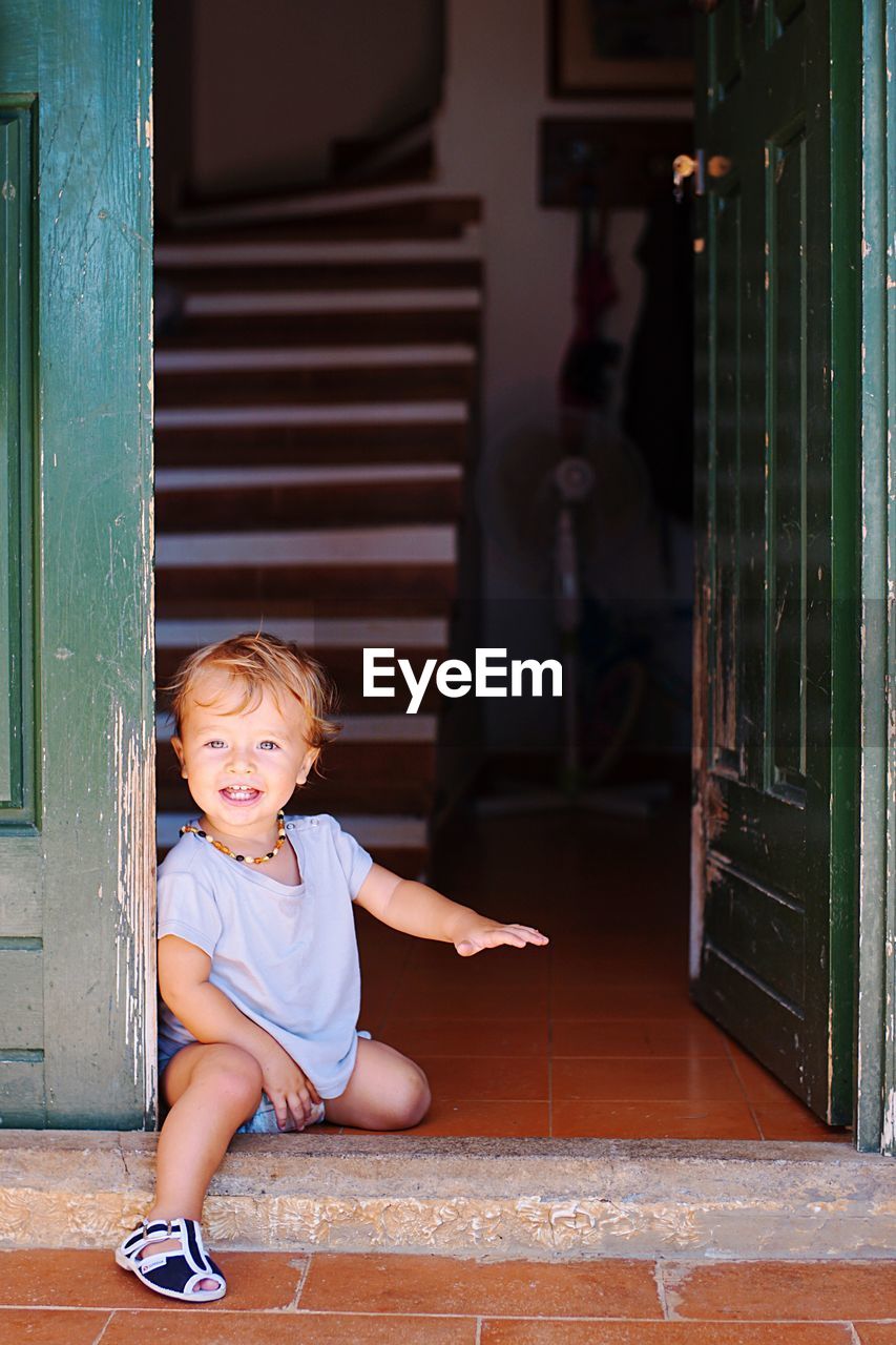 Full length of cute boy sitting at door of house