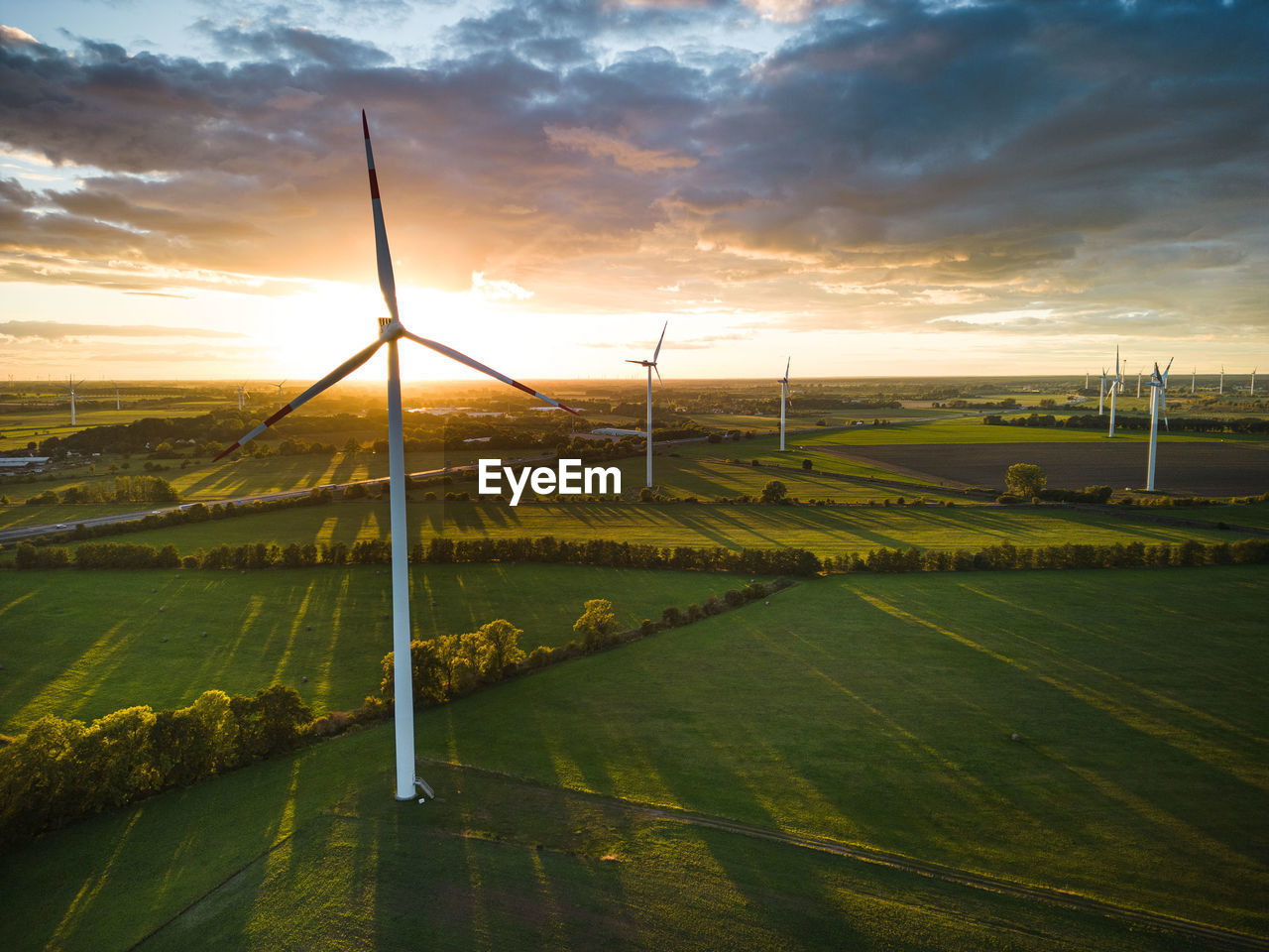environment, sky, environmental conservation, landscape, sunlight, sunset, wind turbine, turbine, wind power, horizon, renewable energy, cloud, nature, beauty in nature, rural scene, agriculture, field, land, power generation, alternative energy, scenics - nature, farm, windmill, sun, plain, tranquility, grass, wind, social issues, no people, technology, dusk, dramatic sky, tranquil scene, plant, outdoors, rural area, sustainable resources, wind farm, twilight, travel, electricity, idyllic, cloudscape, non-urban scene, transportation, evening, yellow, power in nature, water, environmental issues, crop, power supply, sunbeam, reflection, hill, light, green, horizon over land, lens flare, back lit, moody sky