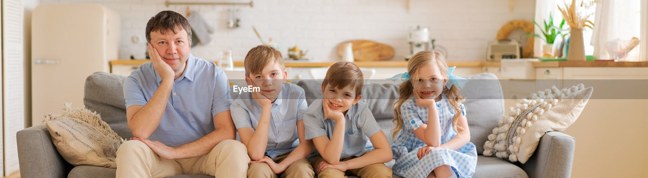 Smiling father with three small children are sitting at home on the sofa