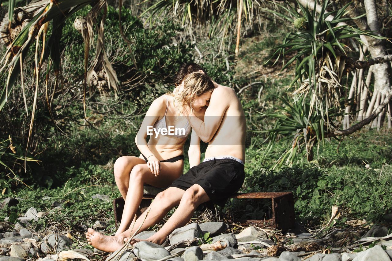 YOUNG COUPLE SITTING AGAINST TREES