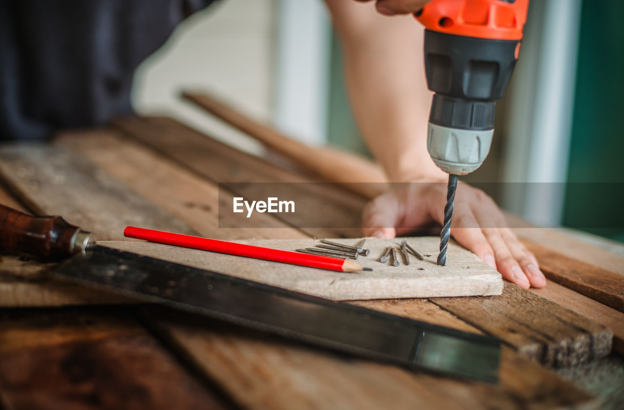 Midsection of man drilling in plank at workshop