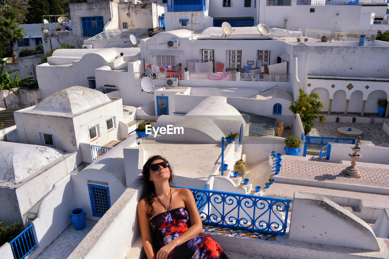 High angle view of mid adult woman wearing sunglasses while sitting on building terrace