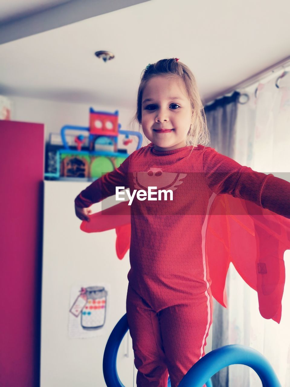 Portrait of smiling girl wearing costume standing with arms outstretched at home