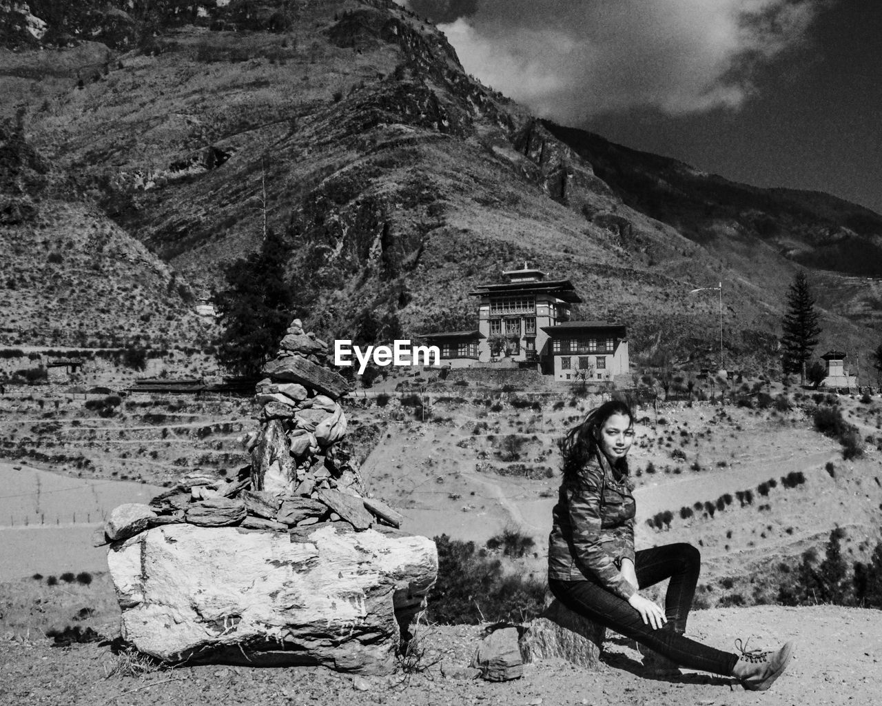 Side view of woman sitting on rock against building