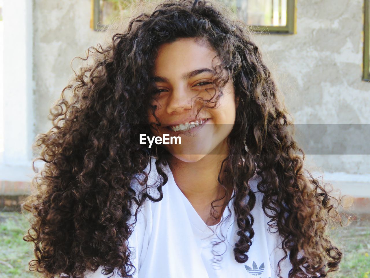 Portrait of smiling teenage girl with curly hair sitting against house