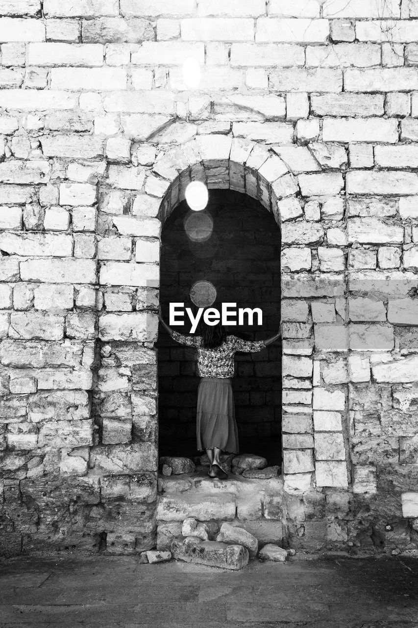 A young woman stands with her back on the ruins of an ancient fortress, black and white photography