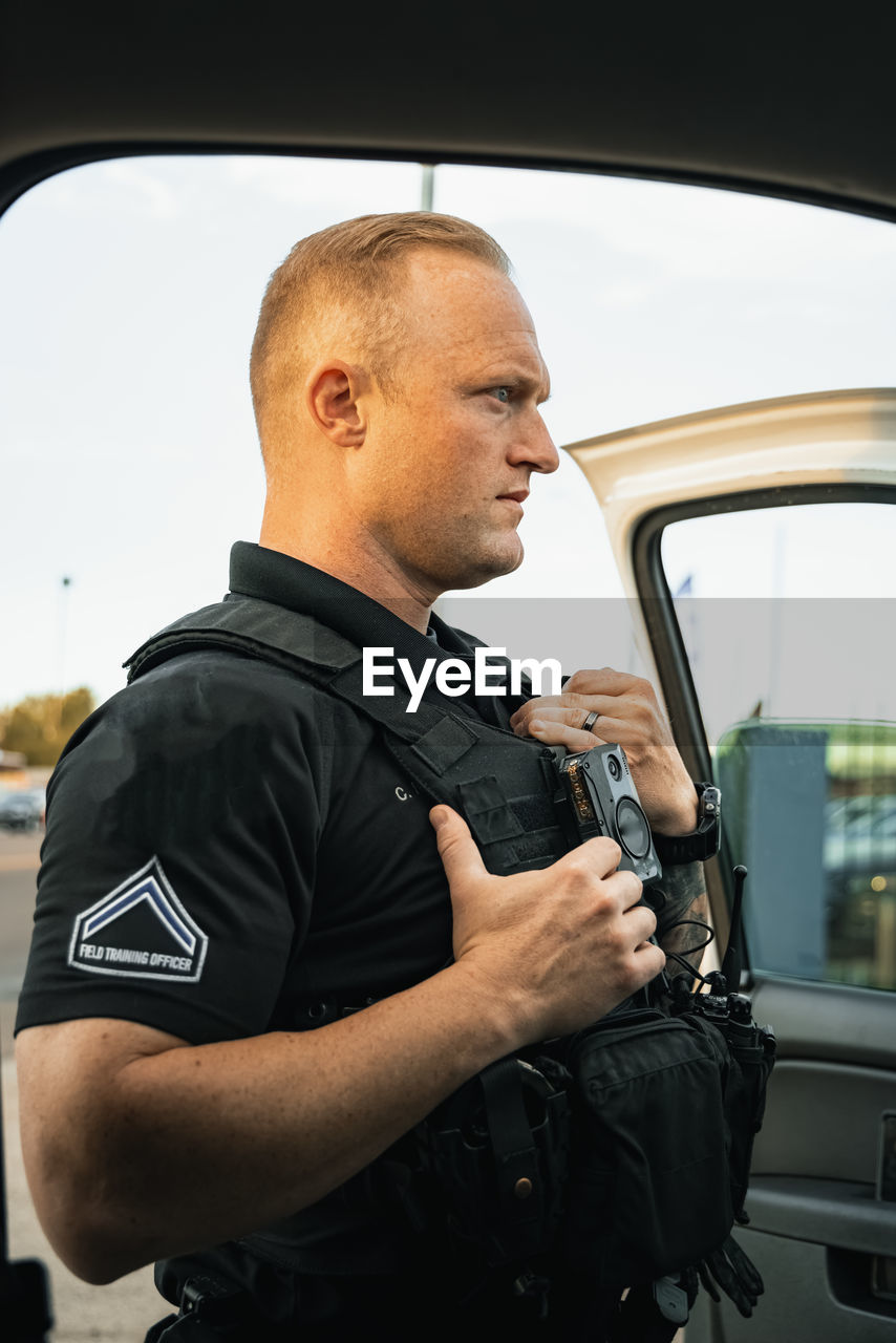 White male police officer standing outside of vehicle to investigate a situation