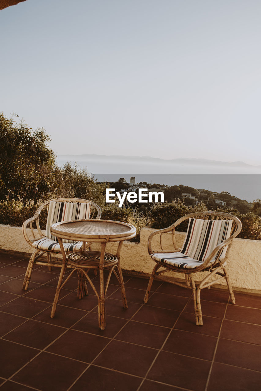 Empty chairs and table by sea against clear sky