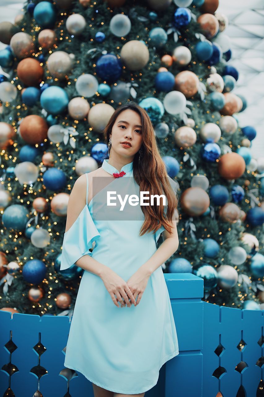 Portrait of smiling young woman standing by christmas tree outdoors