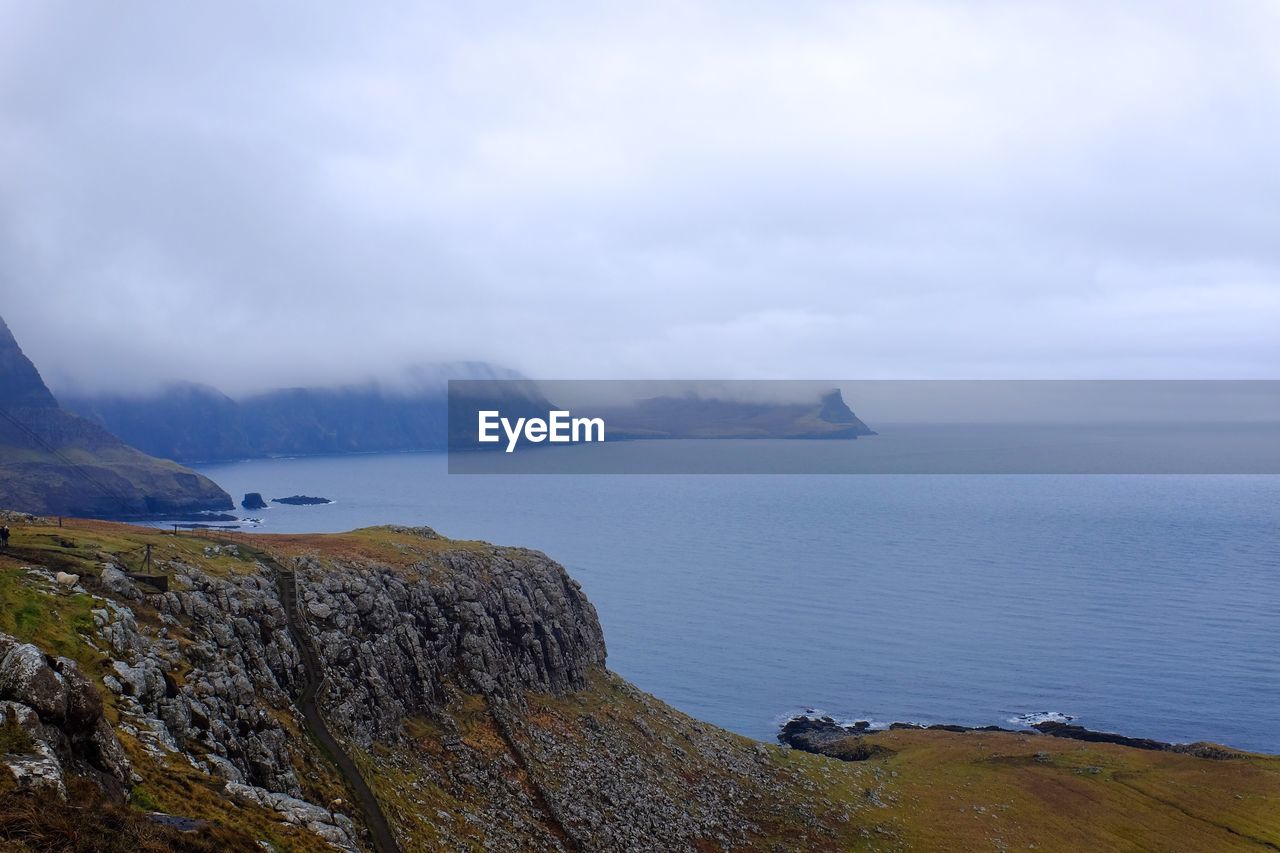 Scenic view of mountains by sea against cloudy sky