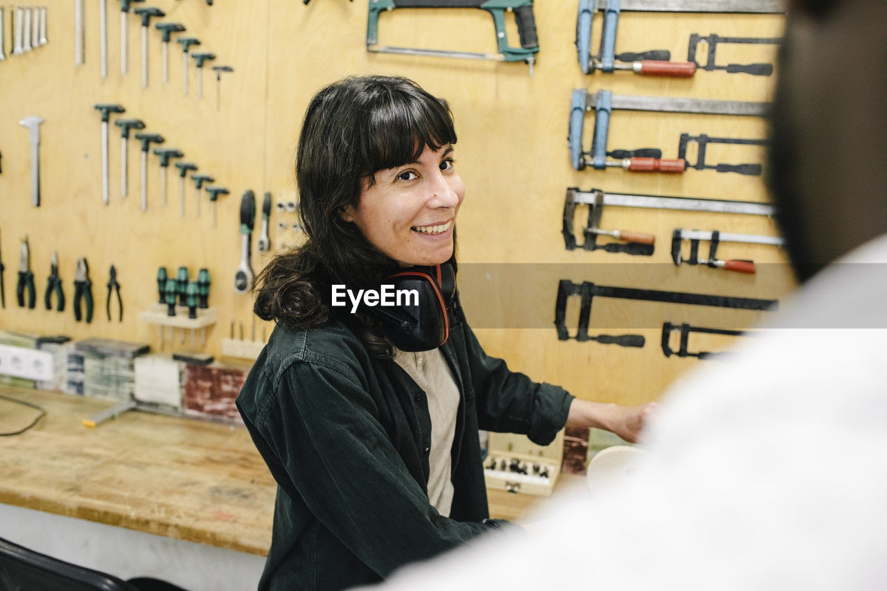 Smiling female technician with ear muffs talking with customer at repair shop
