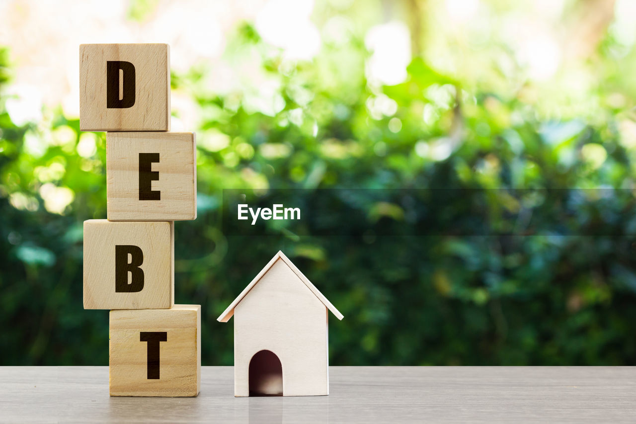 Conceptual about property debt. a small house model with stack of wooden block on nature background.