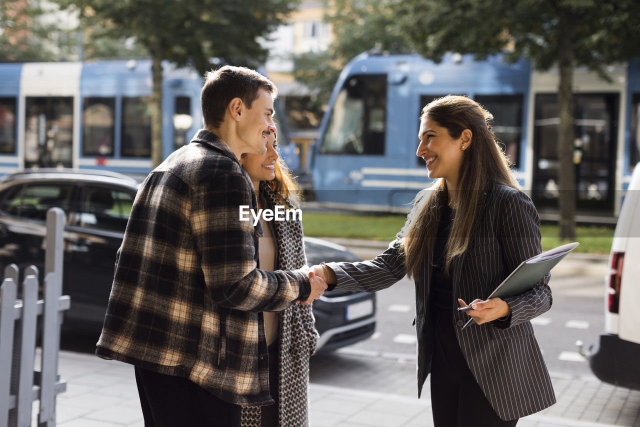 Smiling man doing handshake with female real estate agent while standing at street