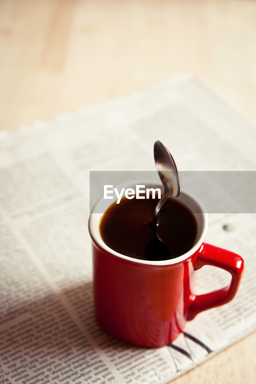 Close-up of black coffee with spoon on newspaper at table