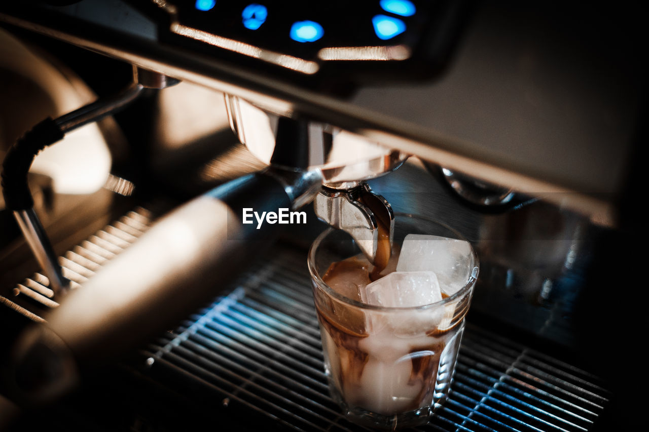 Close-up of coffee pouring in drinking glass at cafe