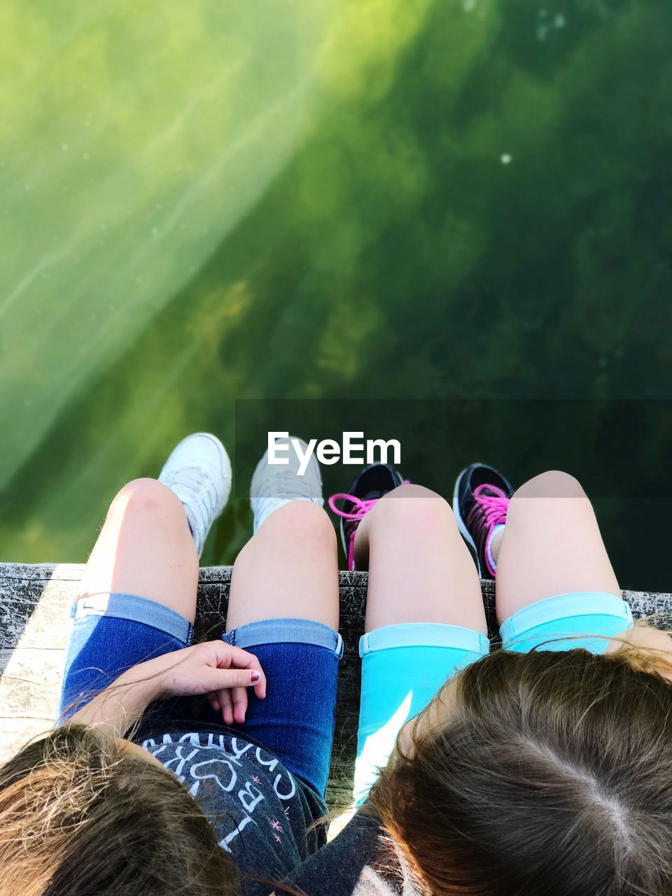 Low section of girls sitting over lake