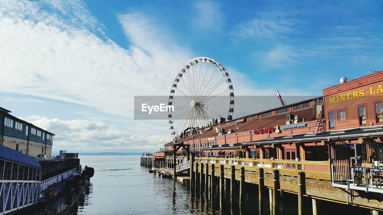 Ferris wheel by pier over sea against sky