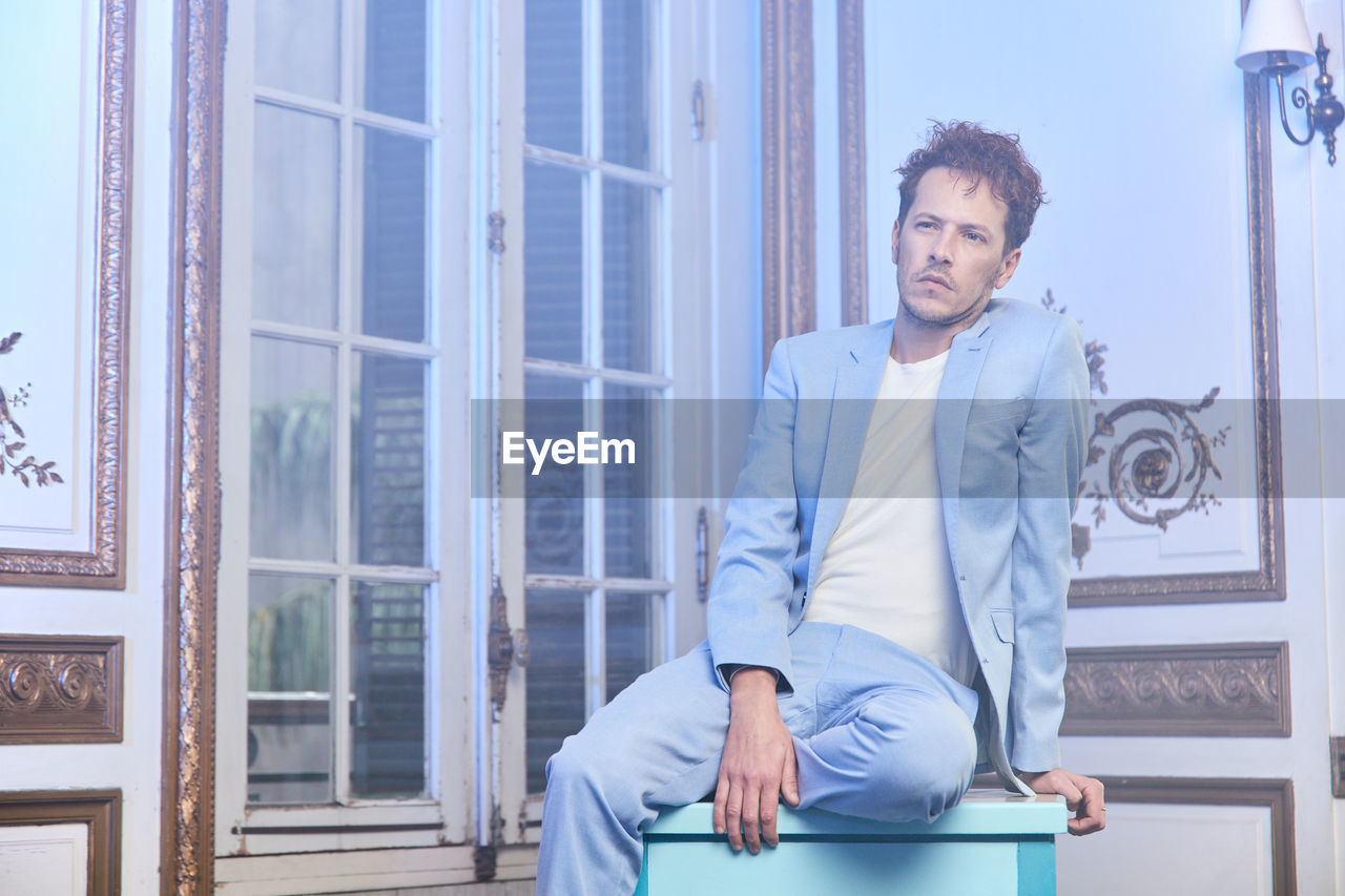 Thoughtful stylish male in suit sitting table in posh room and looking away