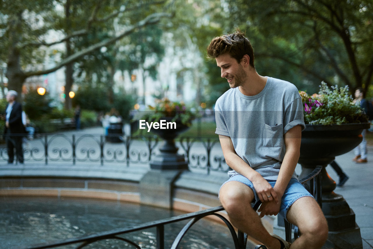 Young man sitting by fountain at park