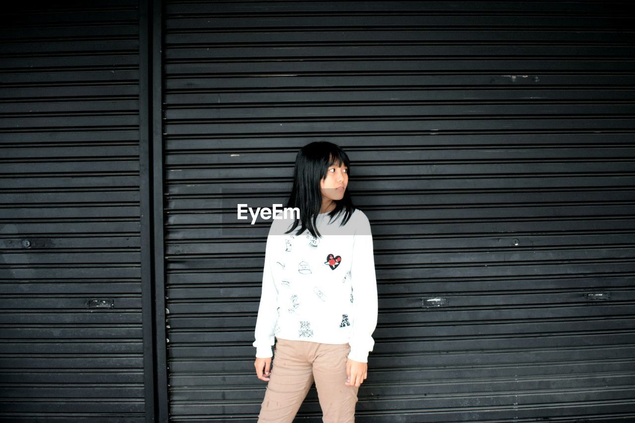 YOUNG WOMAN STANDING AGAINST BLUE WALL