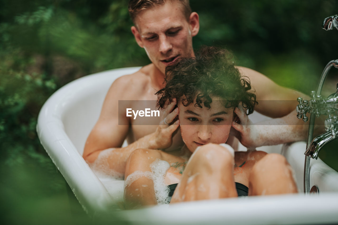 Midsection of shirtless man with woman in bathtub