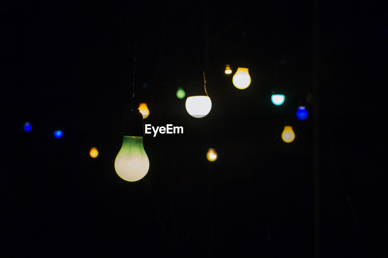 Close-up of illuminated colorful light bulbs hanging in darkroom