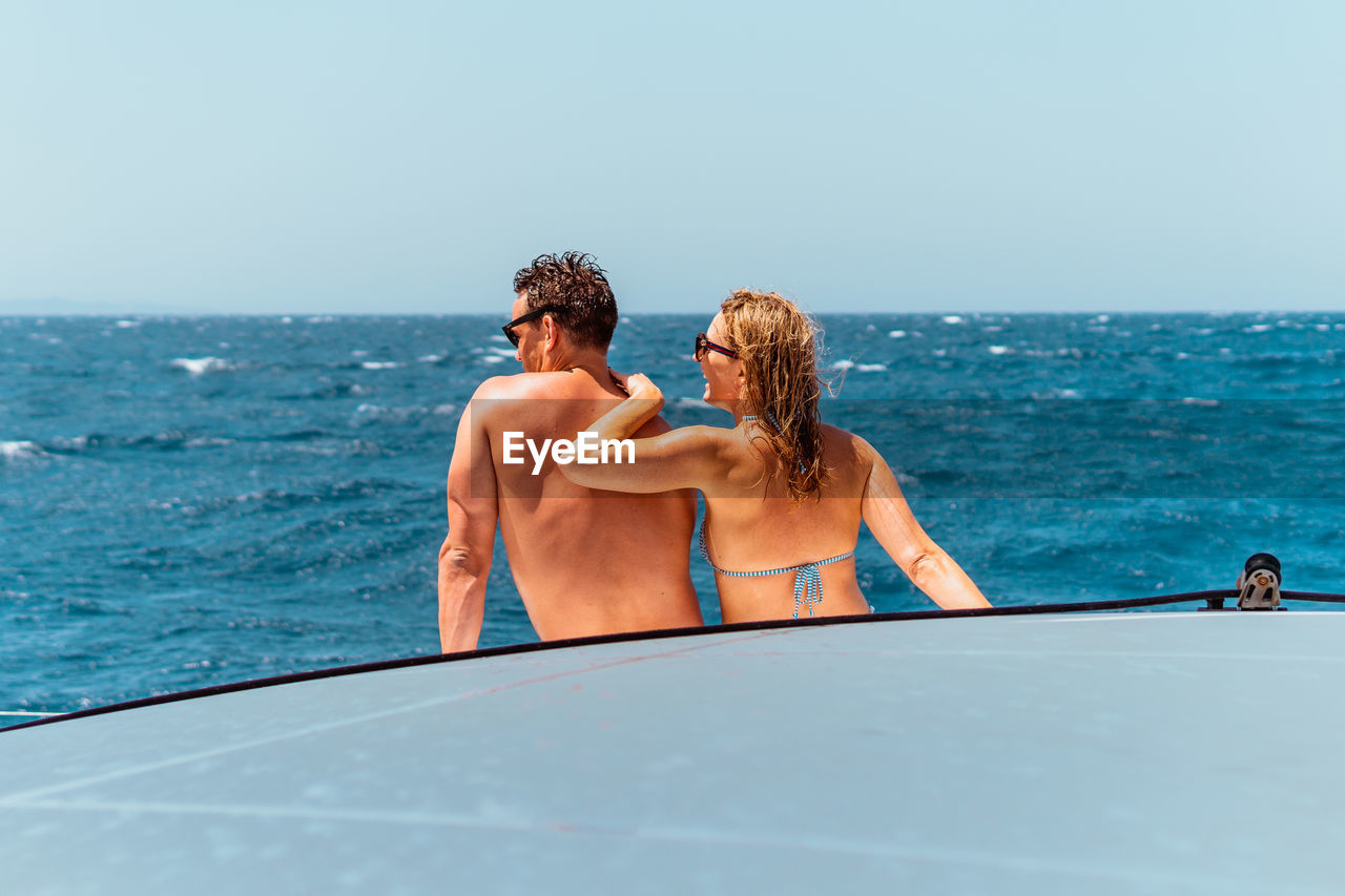 A couple smiling and enjoying vacation on a sailboat in the mediterranean.