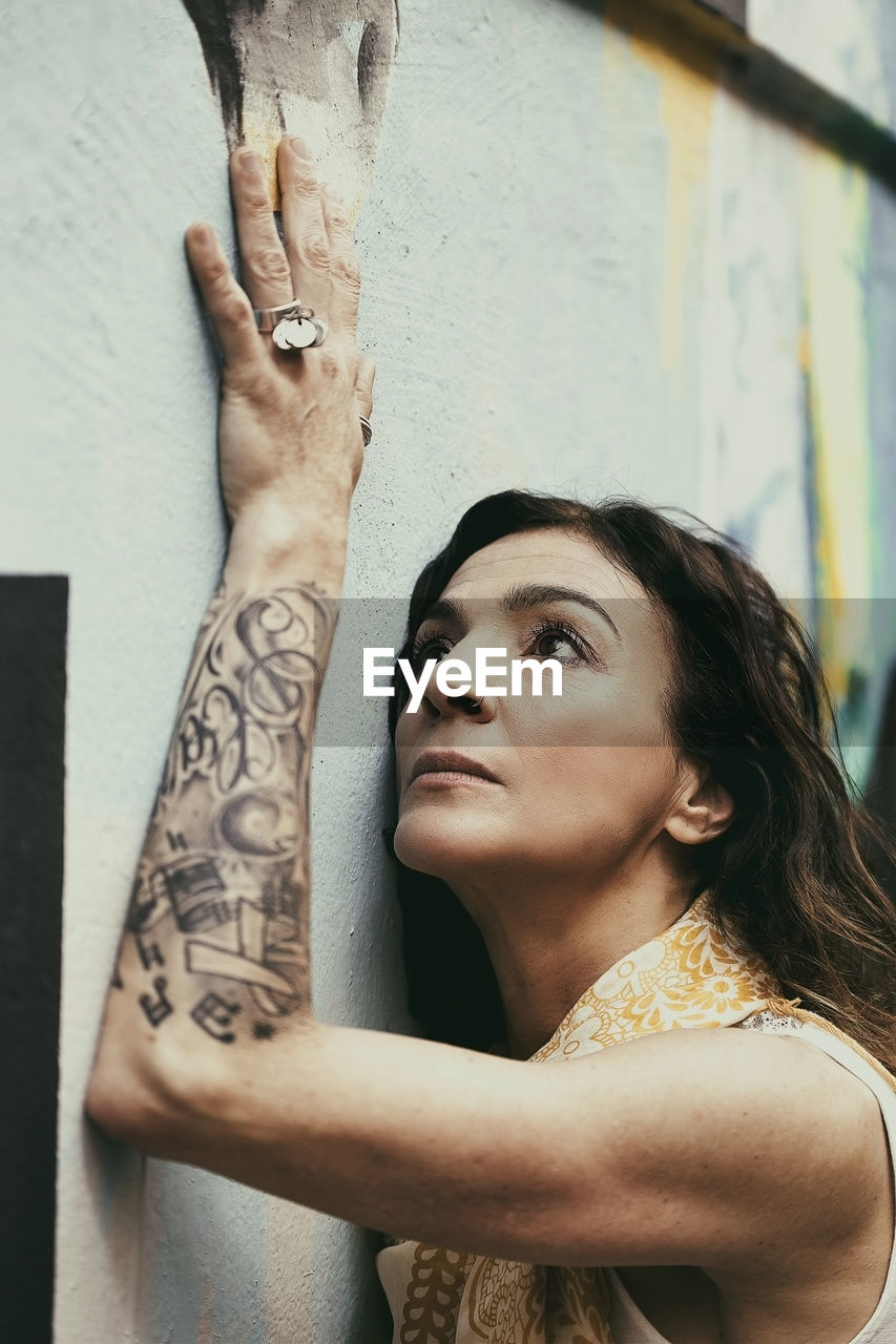 Woman looking away while standing against wall