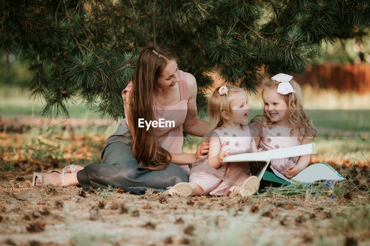 Smiling woman looking at daughters sitting on land