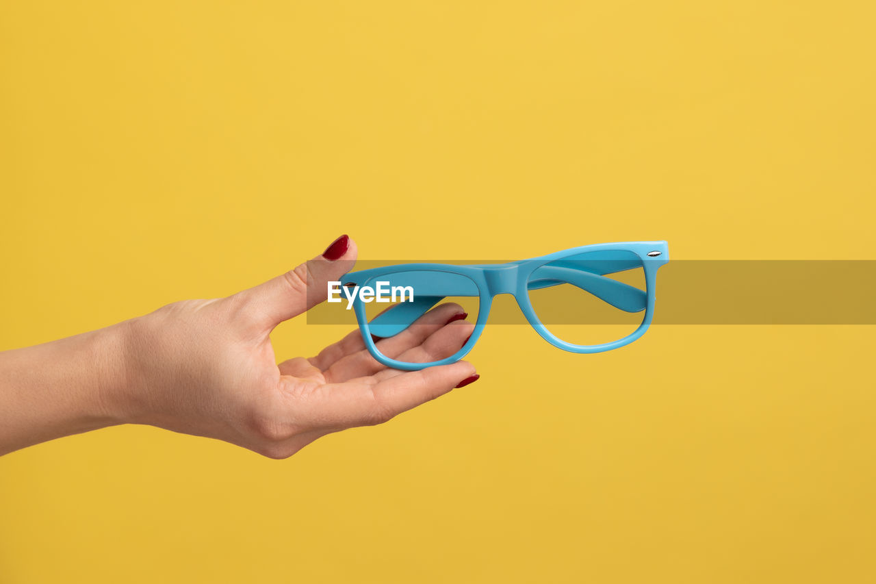 cropped hand of woman holding sunglasses against yellow background