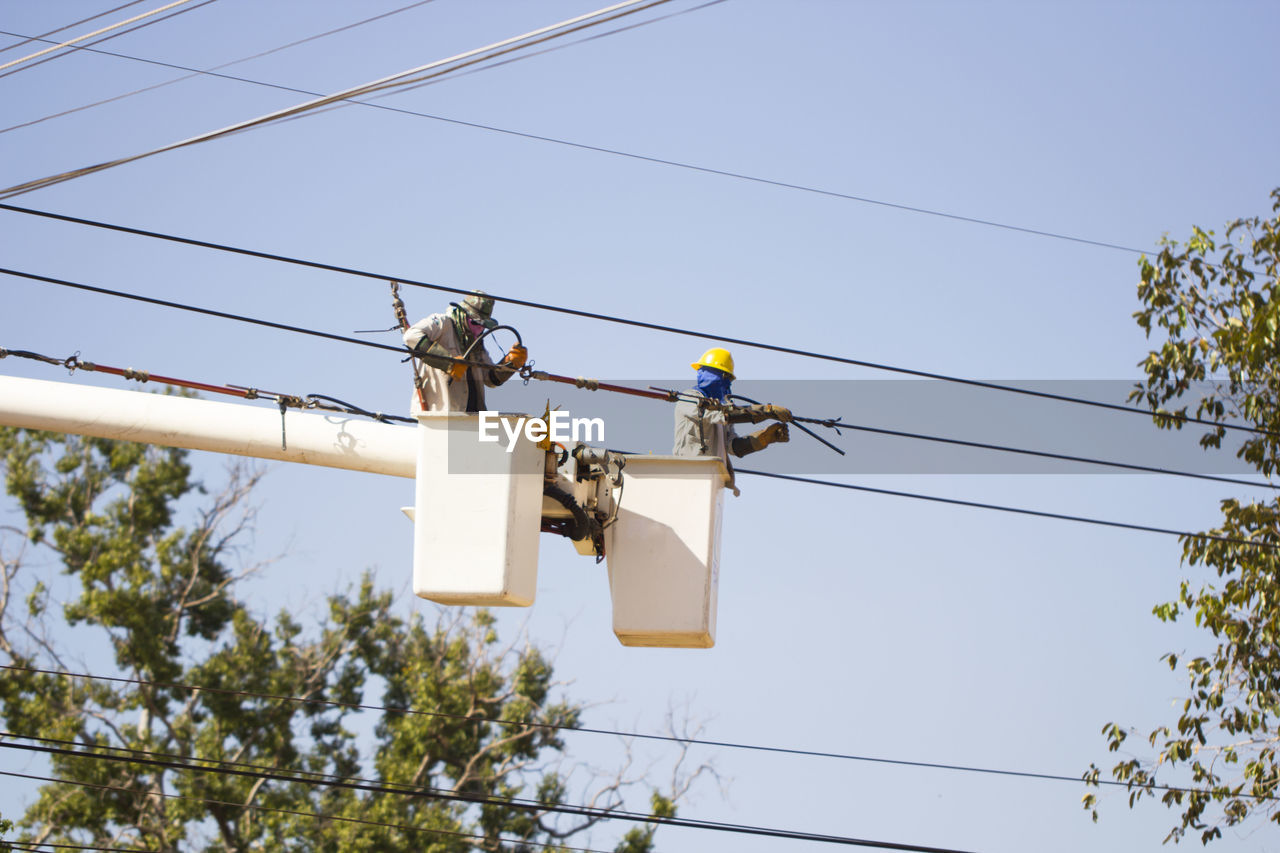 Low angle view of workers in cherry pickers repairing power line