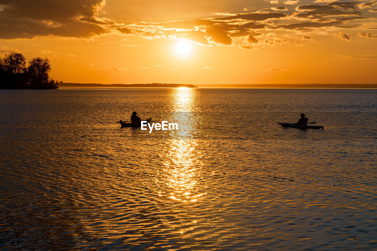 Silhouette people in sea against sky during sunset