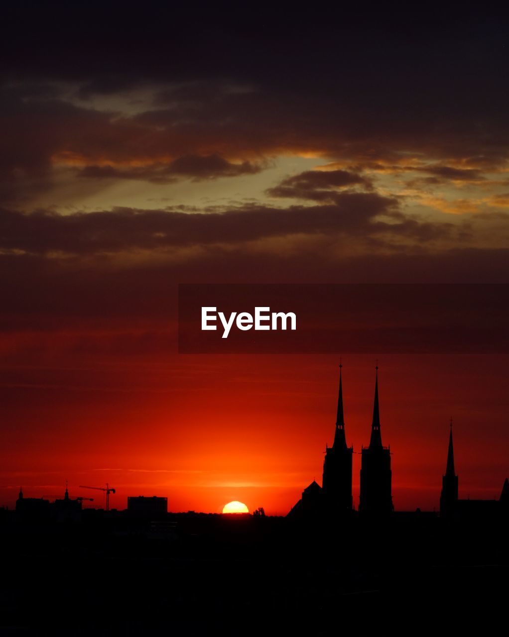 Silhouette of buildings against cloudy sky at sunset